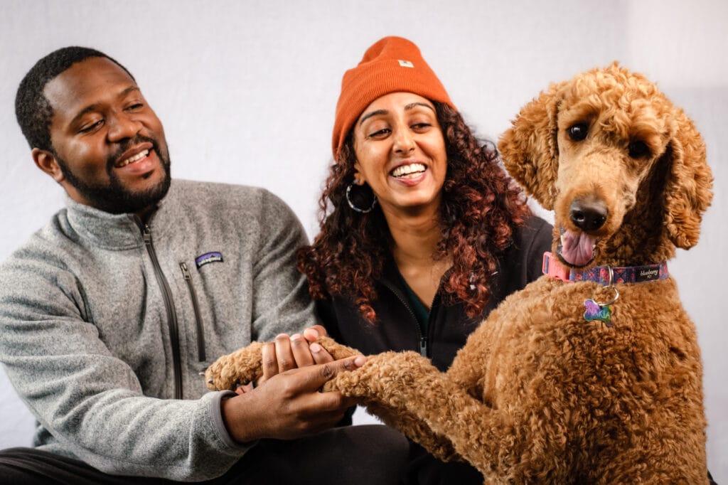 A couple shake hands with their golden doodle dog.
