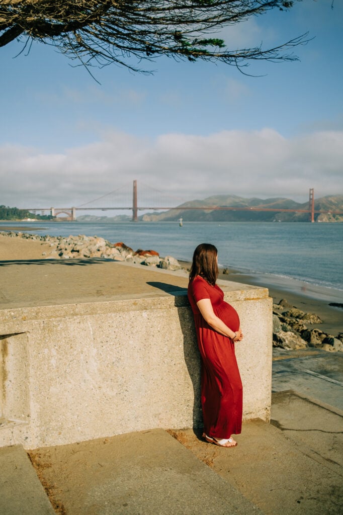 Pregnant woman stands below tree in front of Golden Gate Bridge