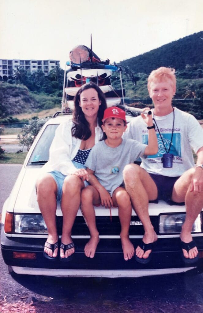 Grainy film photo of family sitting on a car hood, windsurfers loaded on the rack.