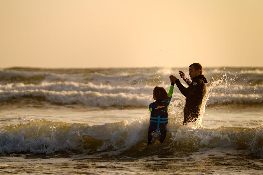 Dad holds son's hand as they jump through an ocean wave.