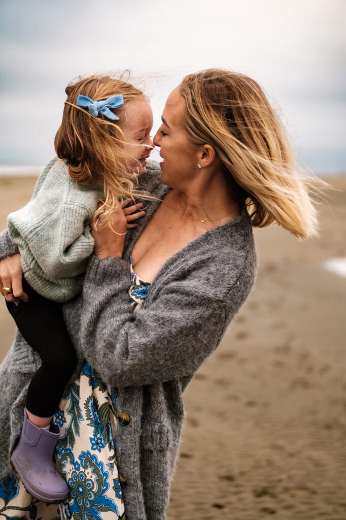 Mom holds daughter as they dance on a windy beach