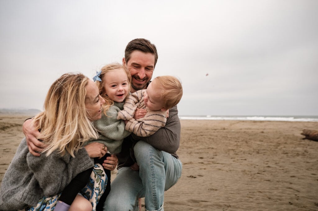 Family of four embrace and laugh on the beach
