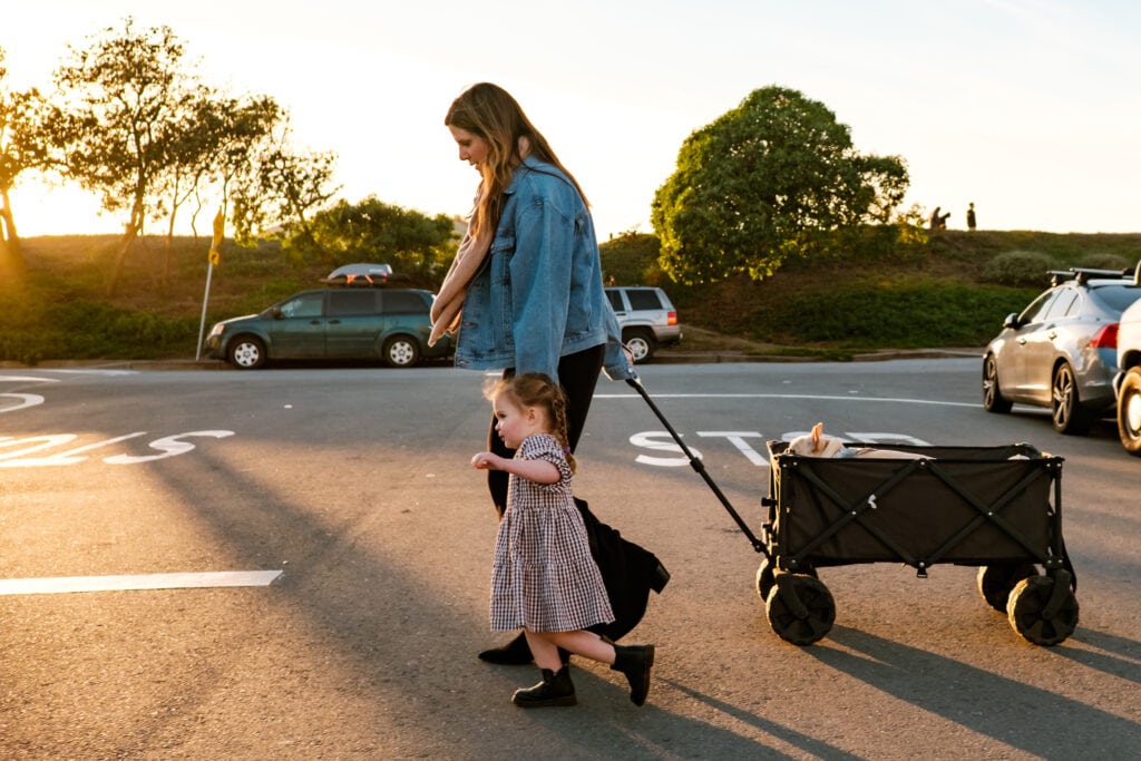 Mom pulls wagon with dog as she walks with daughter across a city street.