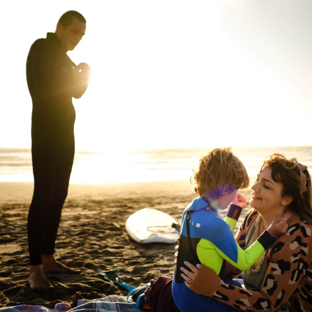 Mom and son have a moment while dad zips his wetsuit to take son surfing
