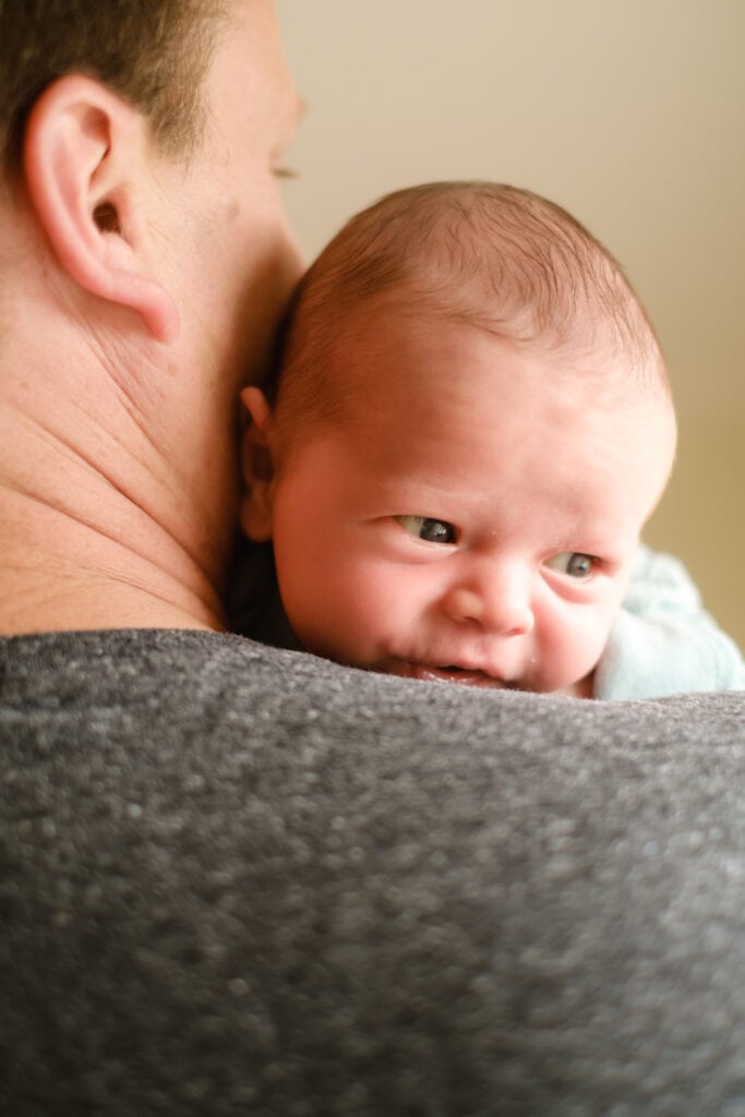 Newborn son looks over dad's shoulder.