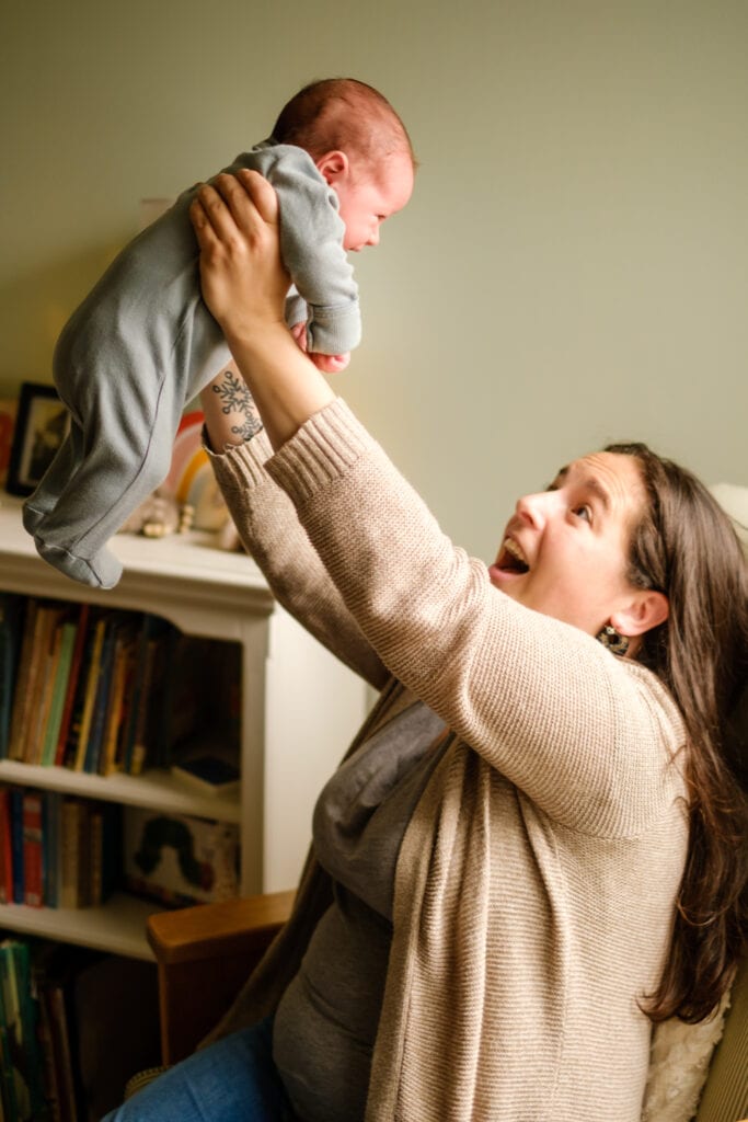 Mother holds her infant son above her head in nursery.