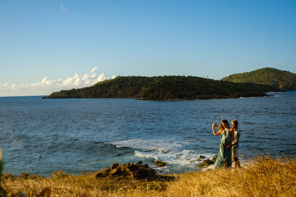 Man and pregnant wife dance on a headland over the ocean.