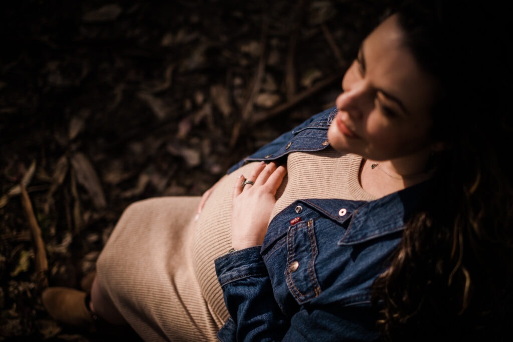 Light filters through the trees onto a woman's pregnant belly