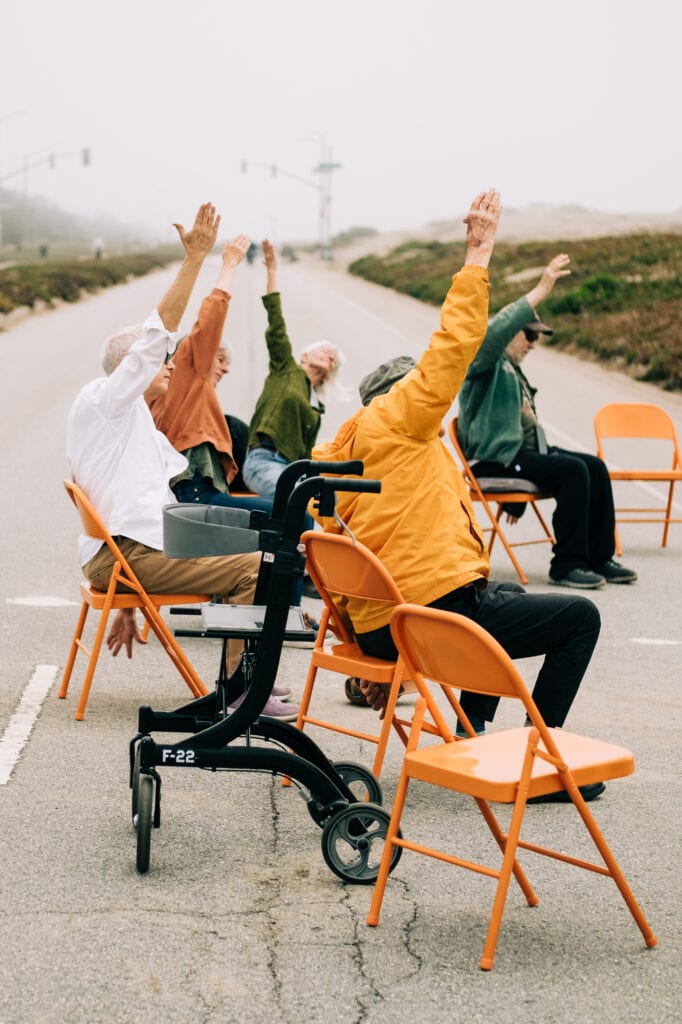 Participants stretch during chair yoga on a roadway turned park
