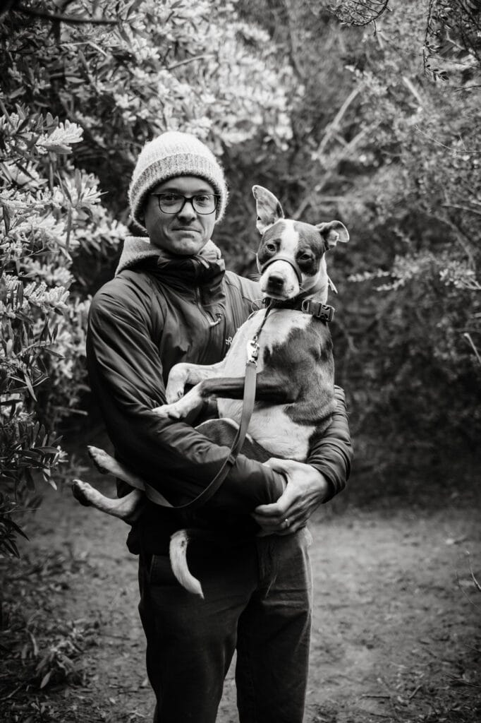 Man holds dog like a baby in a dense tree tunnel.