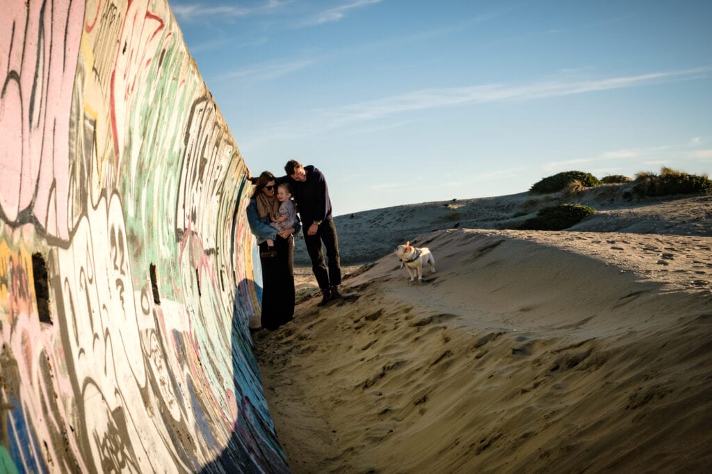Family of three lean against graffiti seawall and look at their dog.