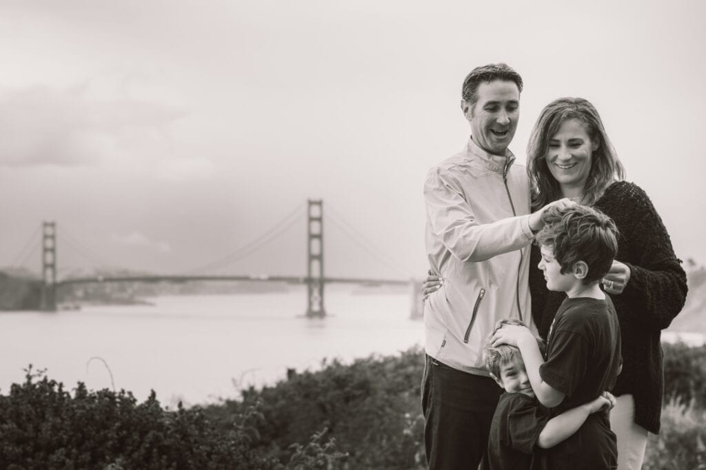 Family of four embrace in front of the Golden Gate Bridge.