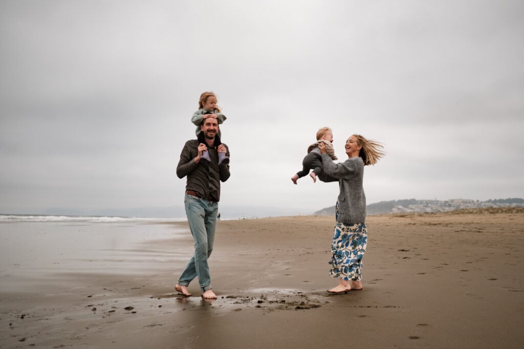 Family of four spin and laugh on foggy beach.