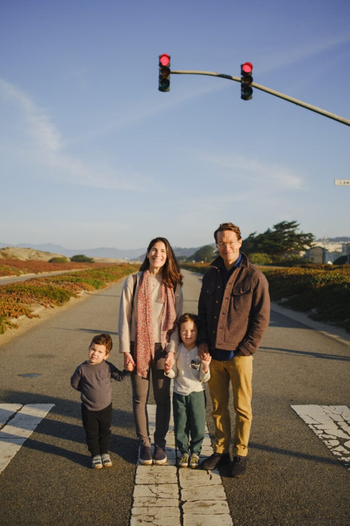 Family of four stand on empty beachside highway in the sun.