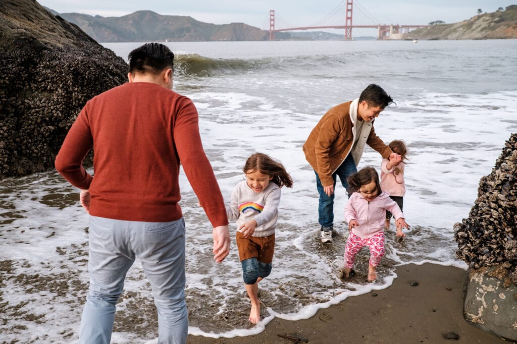 Two dads and three daughters get their feet wet at a beach in front of the Golden Gate Bridge.