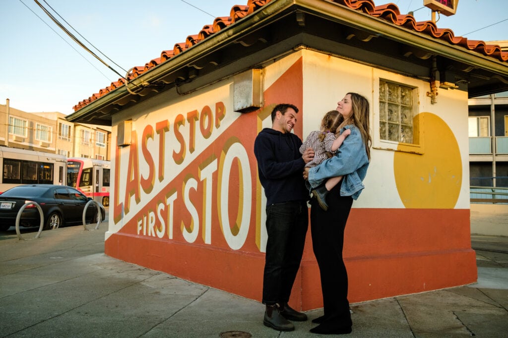 Family embraces in front of famous Outer Sunset San Francisco bus stop mural.
