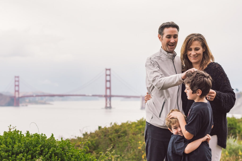 Family of four embrace in front of the Golden Gate Bridge.