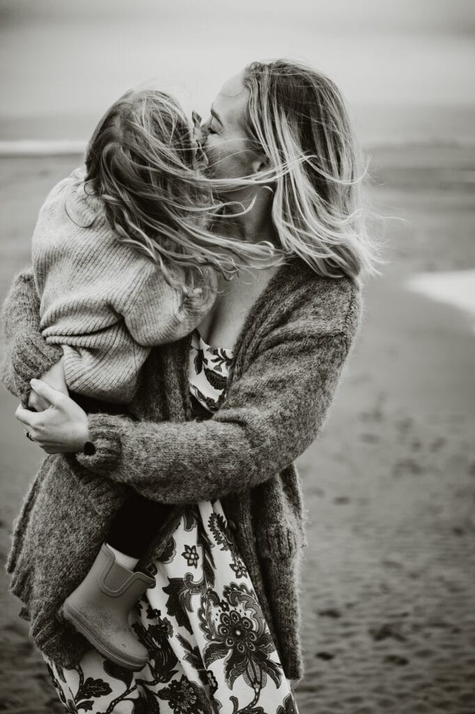 Mom holds daughter and kisses her while wind blows hair.