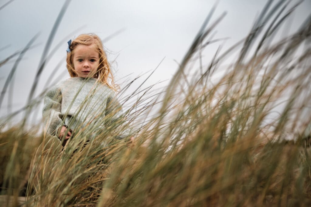 Little girl looking at the camera through sea oat stalks.