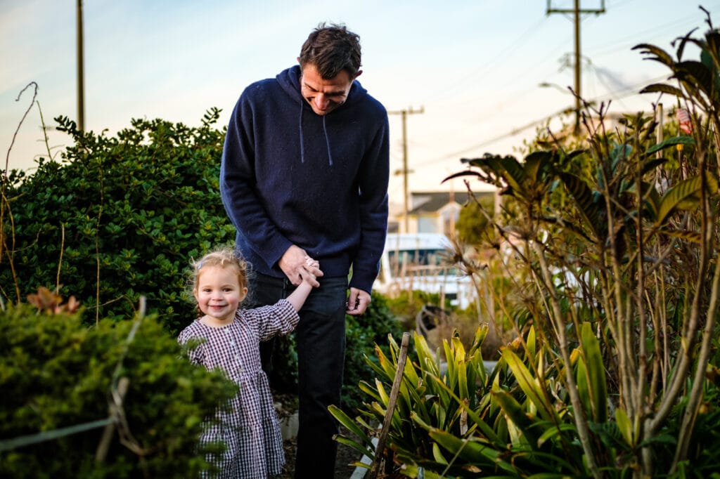 Daughter holds dad's hand and walks him though a garden.