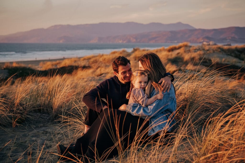 Family embraces amidst sand dune sea oats at sunset.