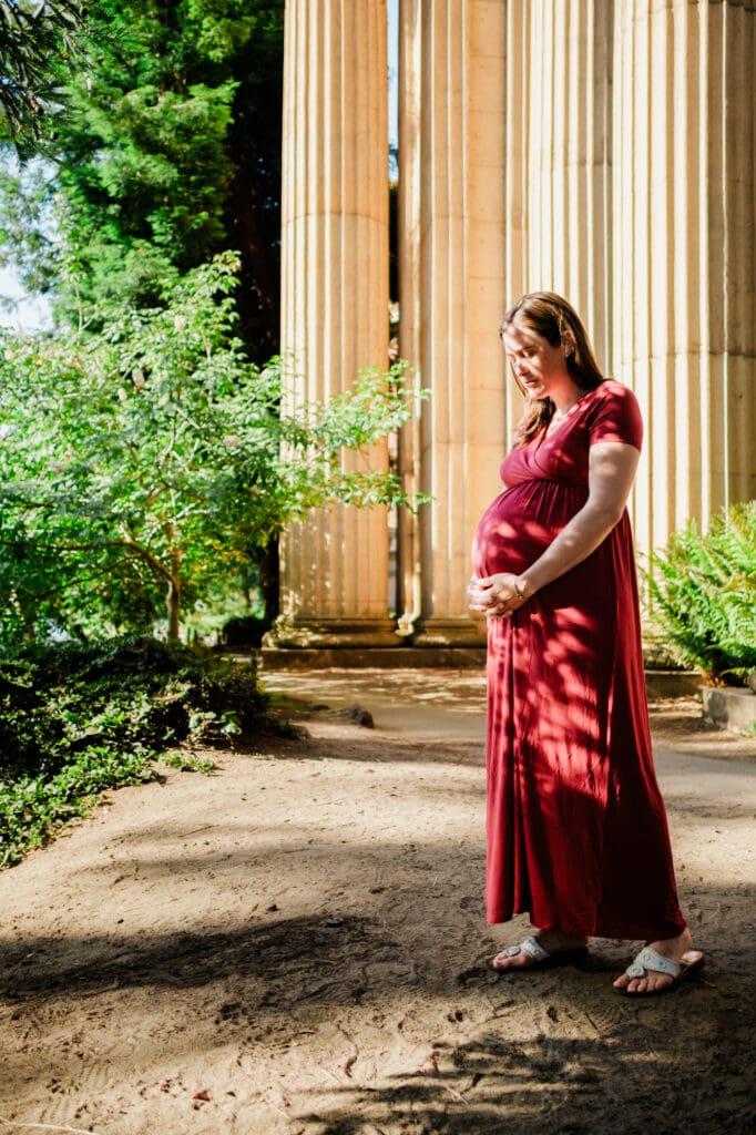 Maternity photo framed by foliage and the pink columns of the San Francisco Palace of Fine Arts.
