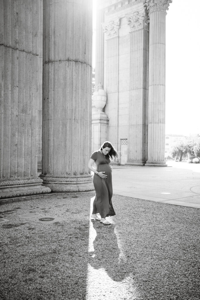 Pregnant woman holds bump in shaft of light streaming between architectural columns