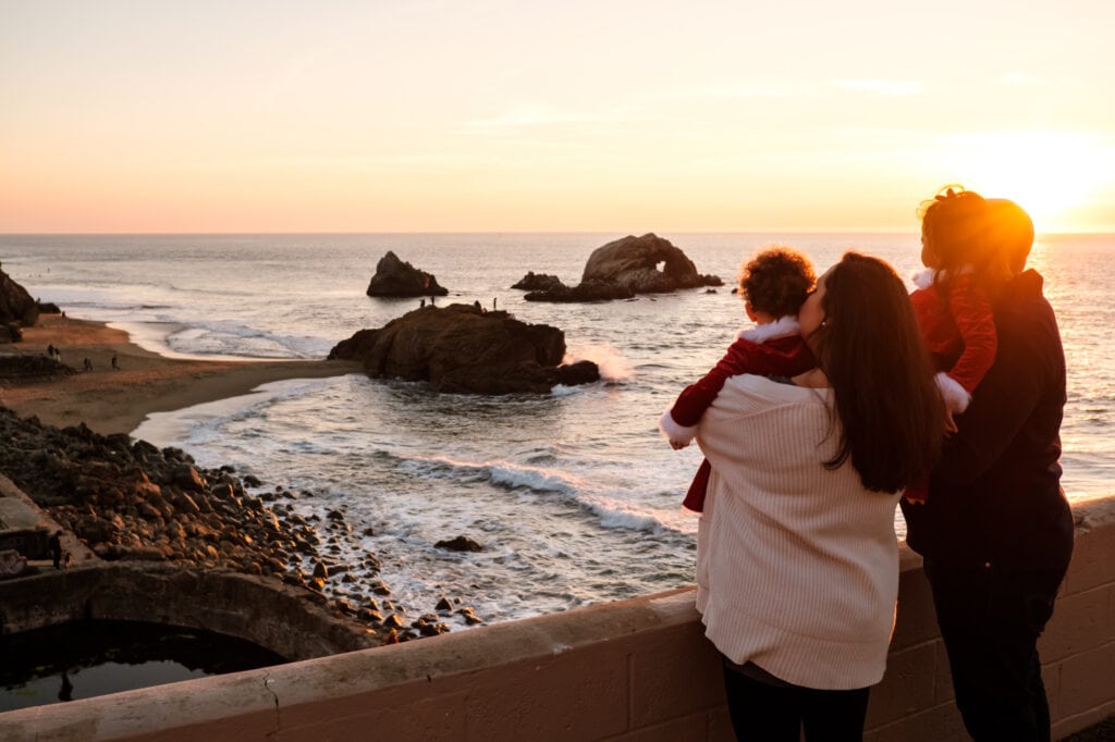 Family of four in golden sunset light look out towards the famous Seal Rocks of Sutro Baths.