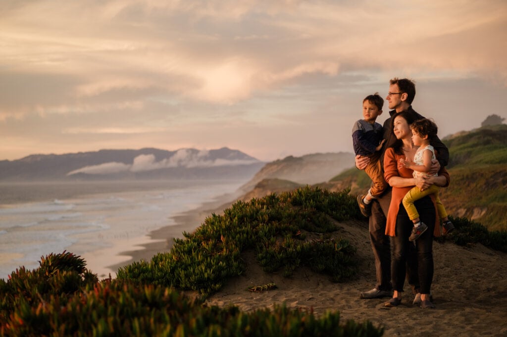 Two parents hold two kids looking out towards a sunset with Marin Headlands in the background.