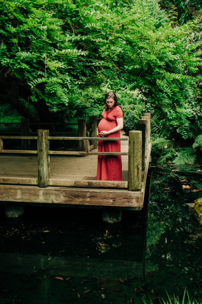 Pregnant woman looks into pond from platform in the forest