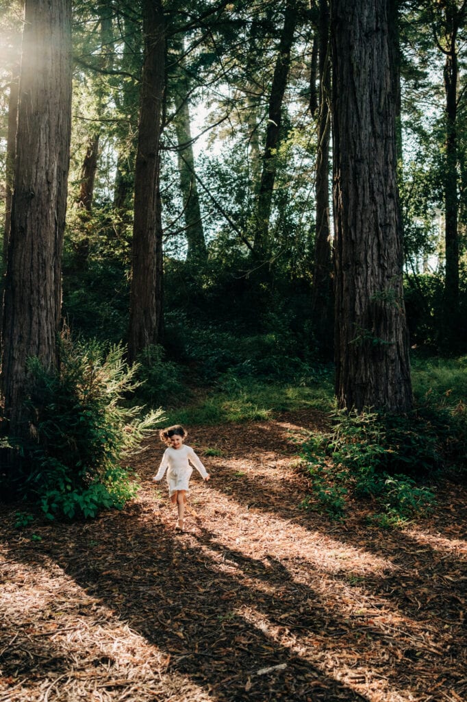 Little girl skips through golden light in a redwood forest.