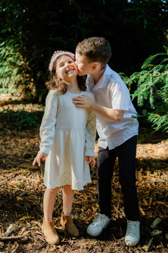 Brother kisses younger sister as she giggles.