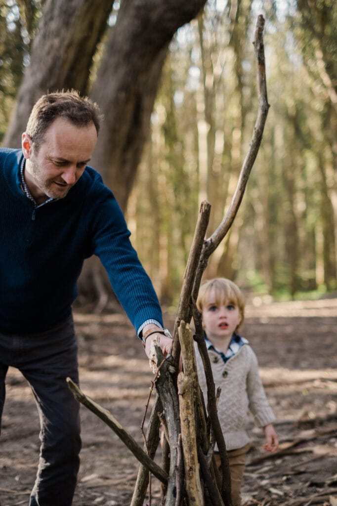 Dad helps son add stick to a lean-to in the forest.