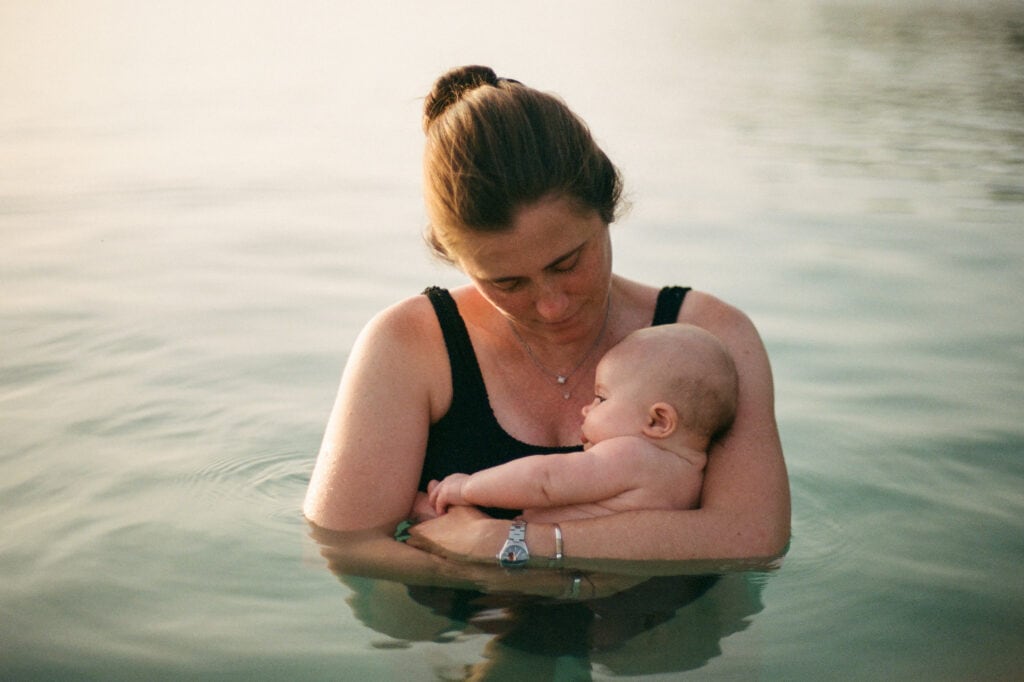 Woman cradles newborn baby while wading in the warm ocean.