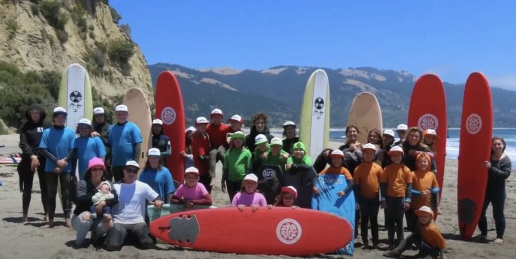 Kids in surf camp pose on a beach with surfboards.