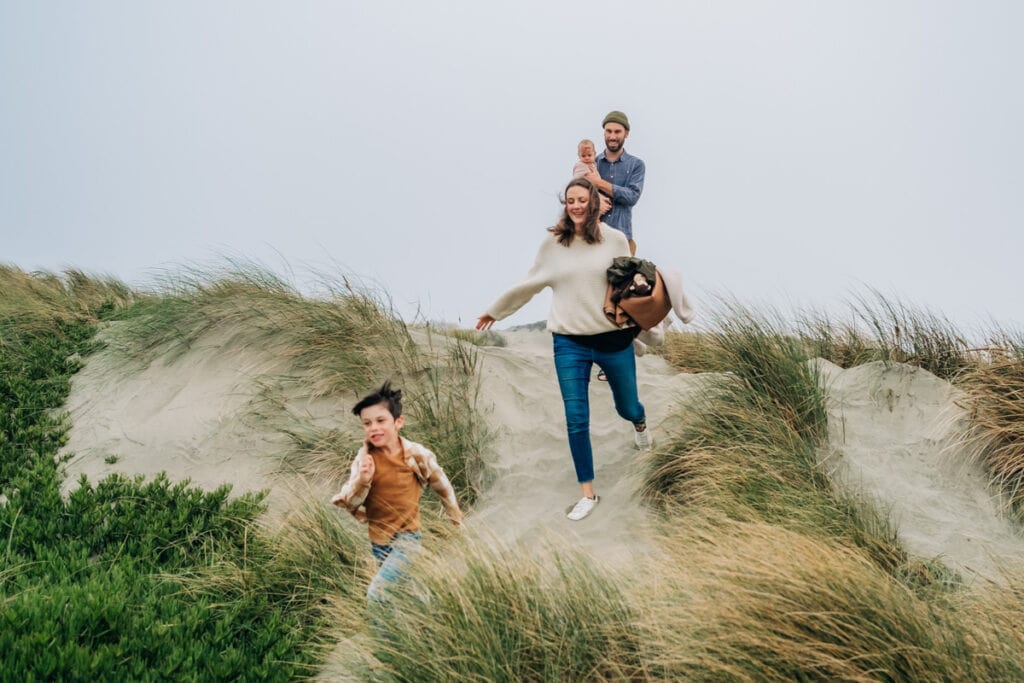 Family of four run together through beach dunes in the fog.
