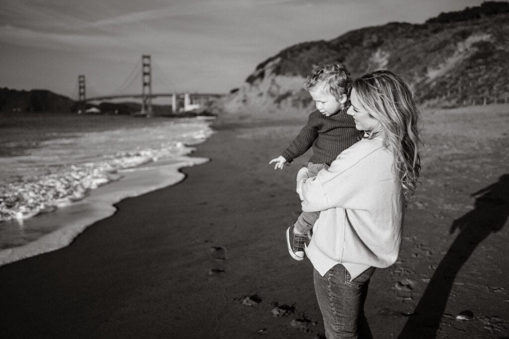 Black and white at sunset of mom holding toddler son in front of the Golden Gate Bridge.