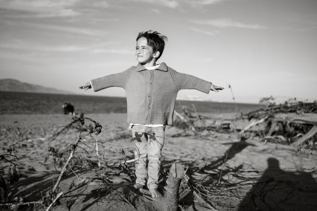 Black and white of boy with his arms behind him as if trying to fly into the sunset.