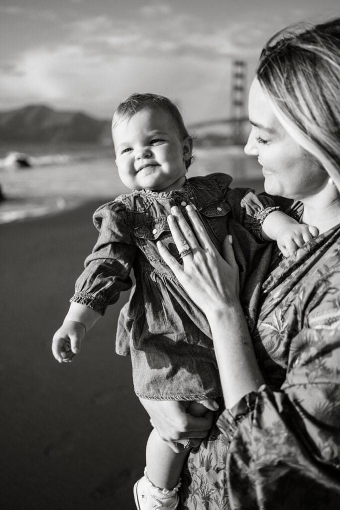 Close up black and white of mom holding baby daughter on a beach in sunset light.
