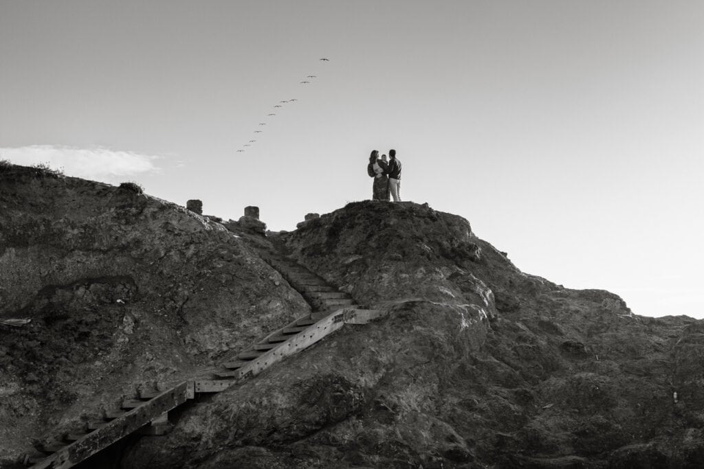Silhouette of family and pelicans standing at the top or a staircase embedded into a rocky peninsula