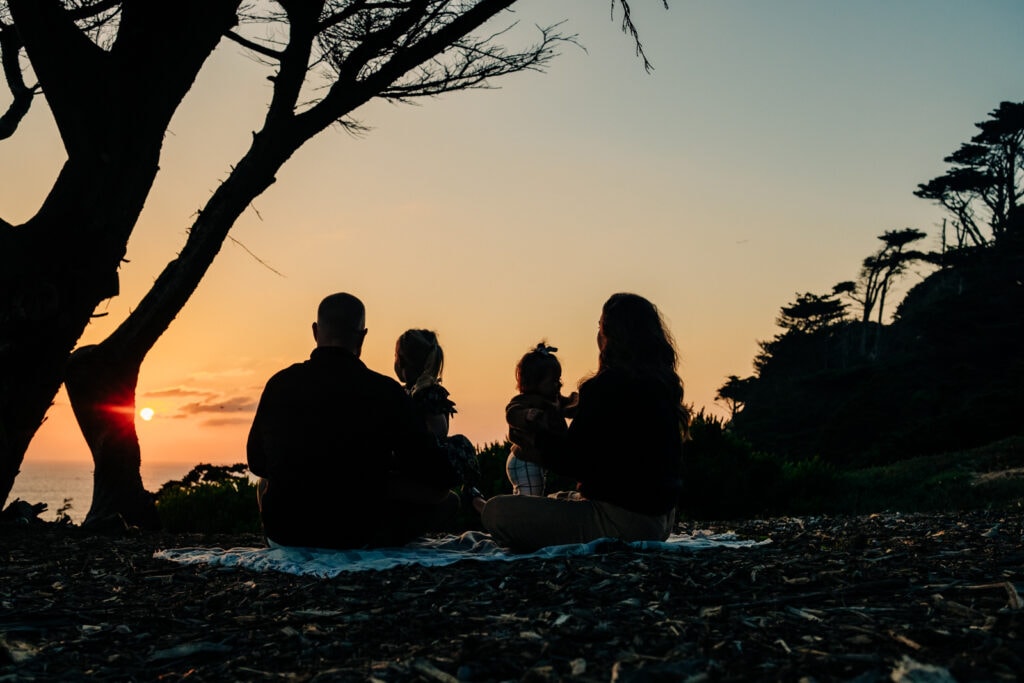 Silhouette of family of four sitting and looking out at the sunset.