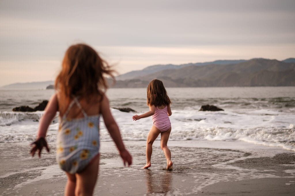 Little girls run into the ocean with the Marin Headlands in the background.