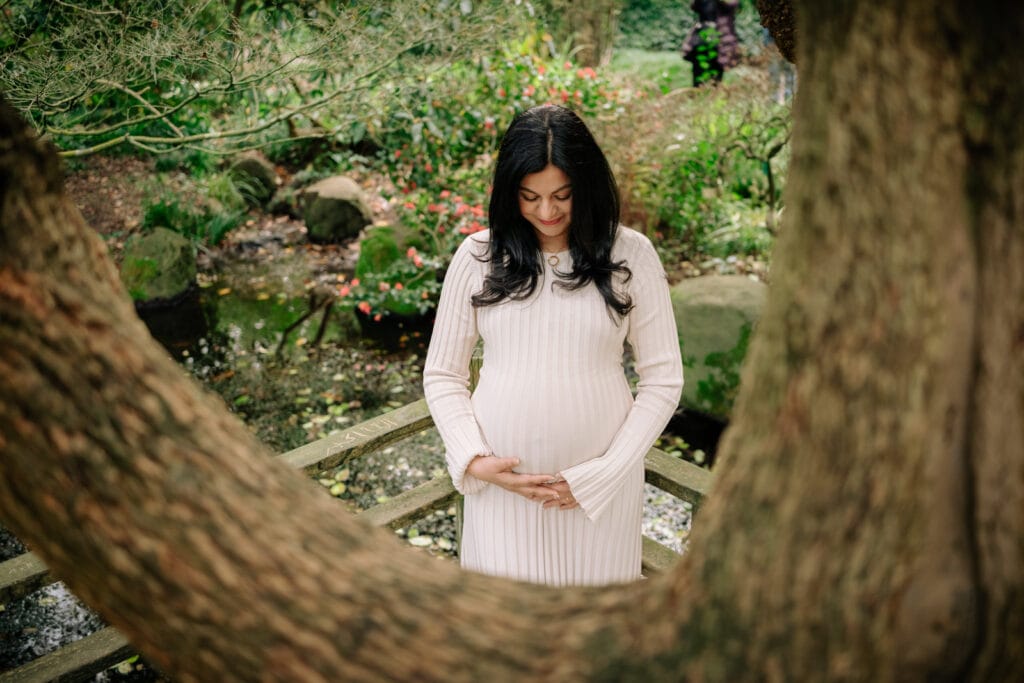 Pregnant woman looking at belly framed in bend of a tree trunk.