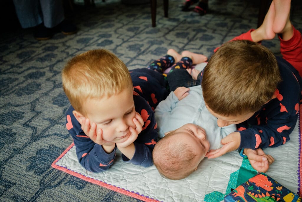 Toddler brothers lay on the floor with a newborn baby