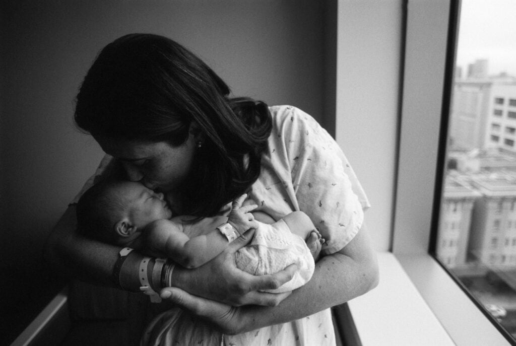 Black and white of mom holding an kissing a newborn in the hospital.