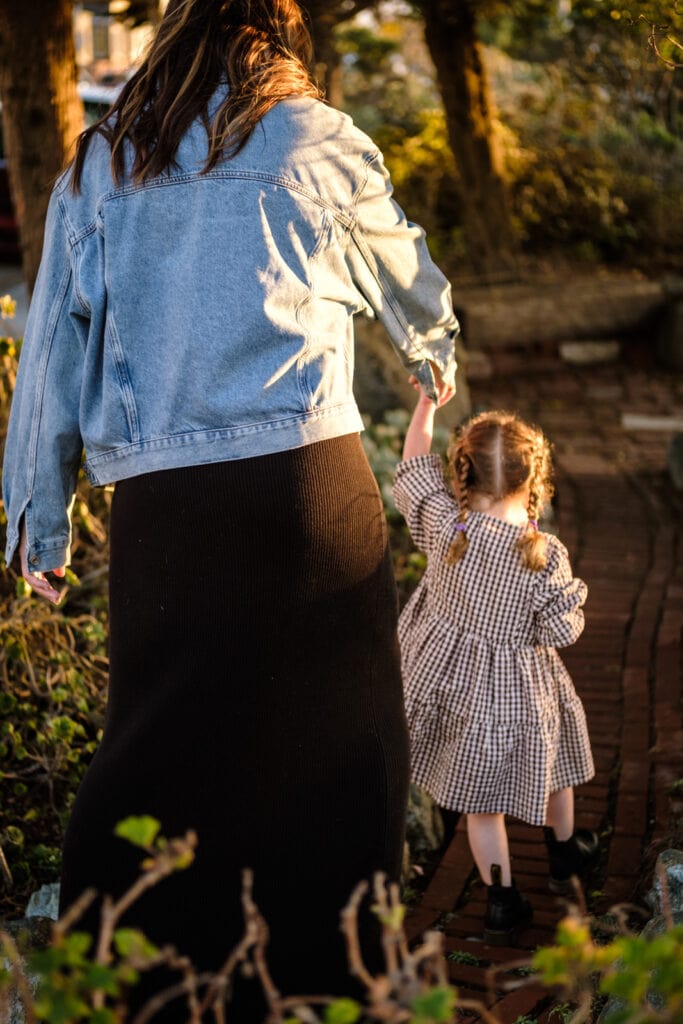 Daughter leads mom by the hand down a garden path.