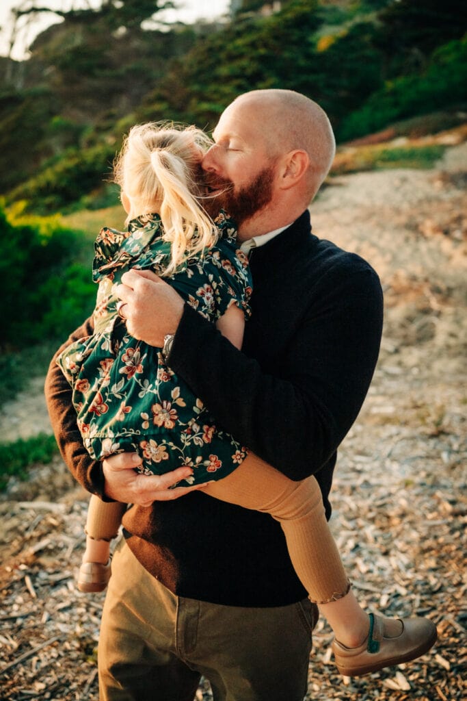 Dad closes his eyes and holds his daughter close in sunset glow.